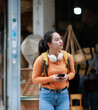 © Tj - Asian woman exploring city with backpack and headphones, looking around while holding smartphone, enjoying travel and leisure during an urban vacation