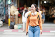 © Tj - Young adult woman traveler with backpack and headphones exploring an urban street market, looking around while walking confidently, enjoying a solo travel adventure and sightseeing