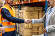 © Koldo_Studio - Two people shaking hands in a logistics distribution center, symbolizing a successful business agreement and partnership