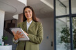 © PeopleVideos - Businesswoman standing in modern office holding a tablet, smiling and looking at camera while working