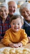 © ISVO - Young boy with Down syndrome in orange sweater smiles while playing with dough in kitchen, surrounded by three smiling elderly adults in casual attire