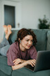 © La Famiglia - Young woman relaxing on sofa working on laptop
