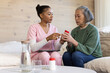 © Wavebreak Media - Diverse female pair, caregiver in pink scrubs using tablet, Senior holding med bottle on sofa