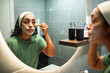 © Marko Geber - Woman applying face mask with brush in bathroom mirror