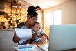 © Marko Geber - Mother paying bills online while holding baby at home