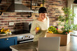 © Davor - Smiling woman unboxing fresh groceries while video calling in home kitchen