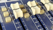 © Maule - Macro shot of white fader sliders on an analog audio mixing console board with decibel level markings.