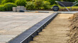 © pufanya - Black recycled plastic paver edge restraint strip anchored in sand on construction site. Landscaping edging system for stone patio installation, professional hardscape project