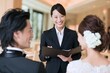 © Jumpei - 笑顔のウェディングプランナーと結婚式の準備相談をする新郎新婦