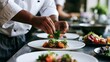 © Thares2020 - A chef carefully garnishes a plated dish with fresh greens and cherry tomatoes on a stainless steel counter
