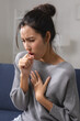© Ratirat - Young asian woman suffering from severe sick cough feeling highly distressed with intense chest pain sitting on sofa looking thoroughly unwell and ill from serious respiratory disease