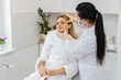 © Andrii Iemelianenko - Middle-aged woman sits in chair while cosmetologist in gloves gently checks facial skin before treatment. Calm adult client in white robe enjoys skincare consultation inside modern beauty clinic room.
