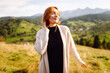 © maxbelchenko - A woman enjoys the mountain scenery on a green hill in the sun's rays. The woman is joyful and feels free standing among the hills and mountains at sunset. Concept of freedom and nature.