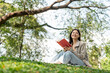 © Chanakon - Young asian woman relaxing reading book sitting at public park life style outdoor. Happy female Take a break enjoy time living in the nature. Human and nature together
