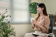 © BTM_Graphic - Young Asian Businesswoman Relaxing with Coffee Cup in Modern Office, Thoughtful and Smiling