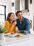 Happy young couple laughing in a modern kitchen. Cheerful man and woman enjoying fresh fruit breakfast together. Relationship and lifestyle concept