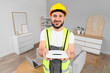 © Pixel-Shot - Smiling male technician in hard hat and safety vest holding a white wi-fi router in a modern home setting