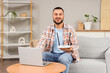 © Pixel-Shot - Smiling young man holding a wifi router and using a laptop on a sofa in a modern living room internet connection, plaid shirt