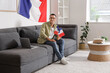 © Pixel-Shot - Young man with laptop and flags of France sitting on sofa at home