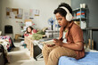© pressmaster - Young boy wearing headphones and using tablet while sitting in temporary shelter, representing displaced family life and digital coping. Ideal for aid, housing, support service campaigns