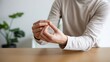 © MSTMAYA - Person rubbing their fingers together while sitting at a wooden table in a bright room indicating anxiety stress or nervous habitual behavior