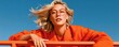© Georgii - Confident young woman in orange blazer and glasses looking upward against a bright blue sky