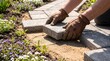 © Mohammad - Professional landscaping worker installing stone pavers, hands in leather gloves laying garden path stones, backyard patio renovation and masonry