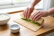 © Stitch - Person rolling a fresh vegetable sushi roll using a bamboo mat on a wooden kitchen counter