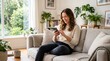 © AKANG - Happy woman relaxing on couch at home using mobile phone for social media