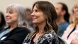 © Thares2020 - A woman with shoulder length brown hair smiles while seated among other attendees at an indoor event