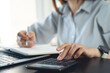© tippapatt - Doing finance, budgeting and tax calculation concept. Woman using calculator to calculate financial report at office desk, accounting with laptop, budget management