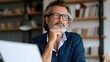 © Thares2020 - A man with glasses and beard sits thoughtfully at a desk  hand on chin  looking upward while reviewing documents