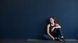 © Juliana - Woman resting after workout sitting on yoga mat against dark blue wall