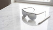 © James - Sunglasses with reflective silver lenses rest on a polished white marble surface next to a sleek pen.