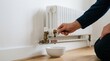 © SimpleDesignStudio - Man bleeding air from a heating radiator with a key into a bowl in a white room