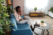 © Marko - Woman talking on phone while sitting in living room with plants