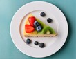 © Kathleen - top view of a single slice of fruit cake served on a white plate topped with fresh strawberries blueberries and kiwi colorful fresh fruit dessert presentation on clean background with soft natural