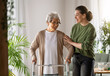 © Konstantin Yuganov - Happy Caregiver Assisting Senior Woman Using Walker in Bright Home