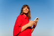 © Nuria Seguí/Stocksy - Beautiful woman in red is using her phone outdoors