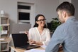 © Prostock-studio - Smiling Latin American Woman Engaging In Conversation While Pointing At Laptop Screen With Male Colleague At Modern Office. Professional Business Concept Focused On Teamwork And Collaboration.