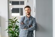 © Prostock-studio - Confident Young Caucasian Man With Neutral Expression Standing With Arms Crossed In Modern Office Environment, Looking Forward. Professional Masculine Presence. Business Concept.