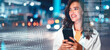 © Prostock-studio - Happy Young Woman Smiling While Holding Smartphone In Urban Environment During Evening, Surrounded By City Lights And Modern Architecture. Engaging With Technology, Urban Lifestyle Concept.