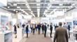 © CuteBee - Business people networking at large corporate trade show exhibition hall with blurred booths and bright overhead lighting in professional business conference event setting