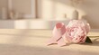 © Akhmad Masudi - Pink Ribbon for Breast Cancer Awareness Month with Peony Flower on Wooden Table in Soft Sunlight
