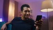 © VAKSMANV - African American guy close-up. Young man is holding gadget with one hand. Boy is starred at smartphone and smiling. Young person at home having chat by phone. Multicultural diversity.