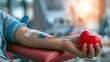 © SSP - A person donates blood, holding a red heart-shaped stress ball while connected to a blood collection needle and tube.