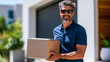 © Nataliya - Man entering his home carrying a delivery box on a sunny afternoon, residential courier service lifestyle, with copy space