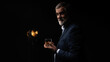 © opolja - Handsome businessman in stylish suit holding glass whiskey on dark