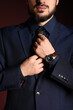 © Pixel-Shot - Businessman with stylish wristwatch adjusting necktie on burgundy background, closeup