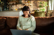 © Davor - Smiling woman using laptop on sofa at home